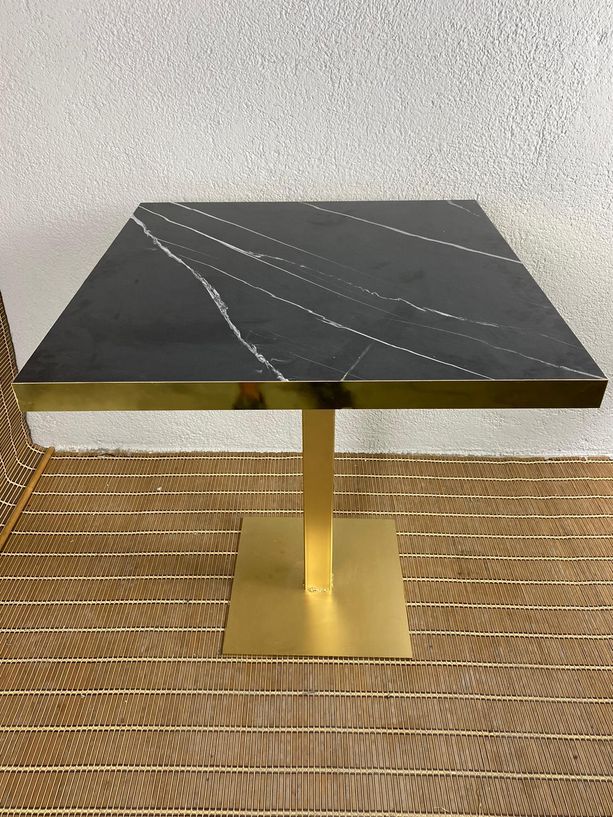 mesa estilo mármol negro con canto de metal dorado y pie de hierro dorado